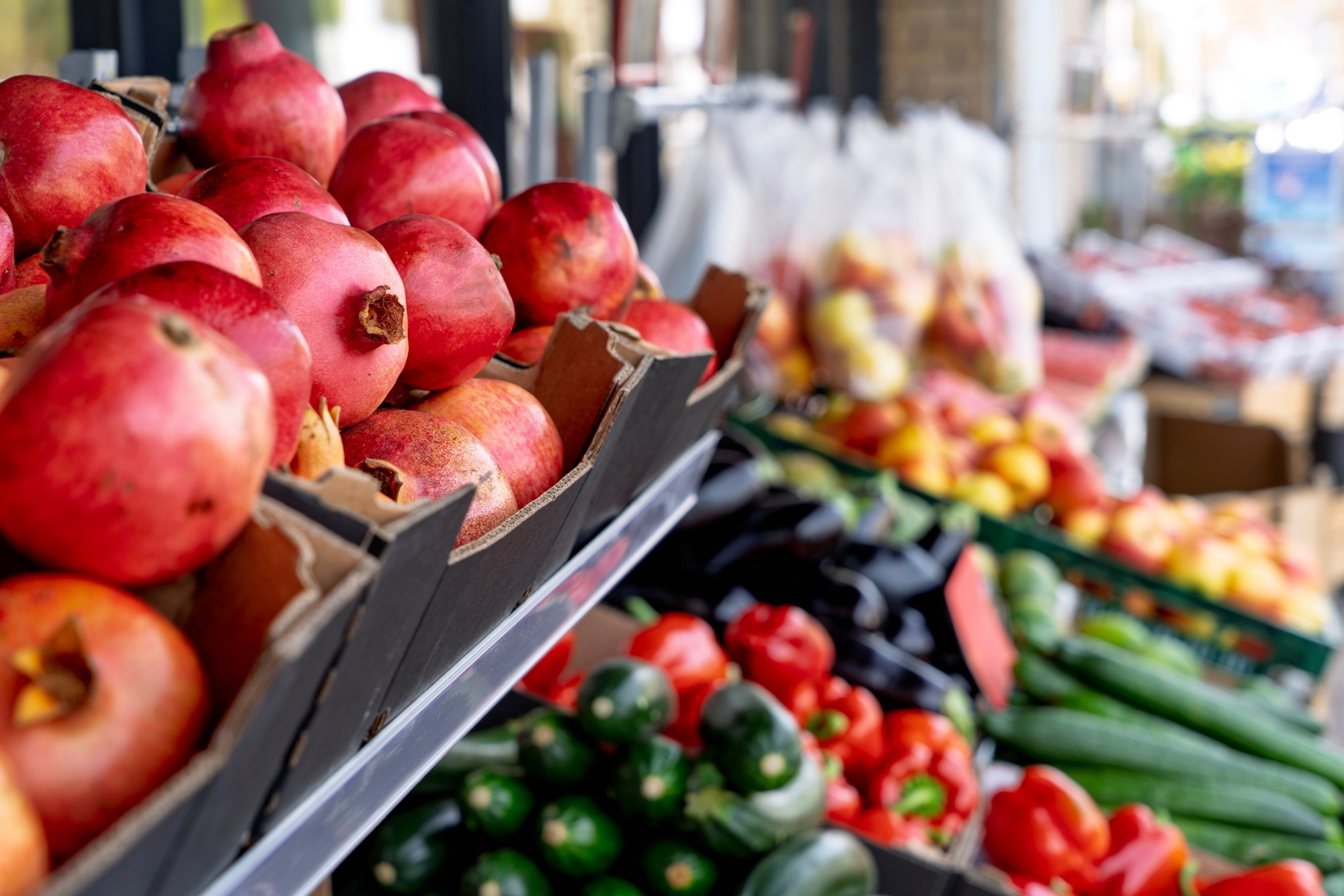 Granaatappels in kratjes, met groente en fruit op de achtergrond