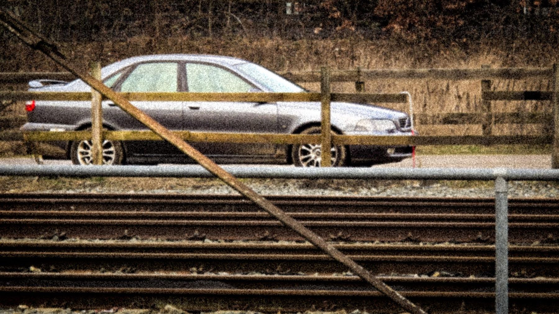 Grijze auto achter een houten hek langs het spoor